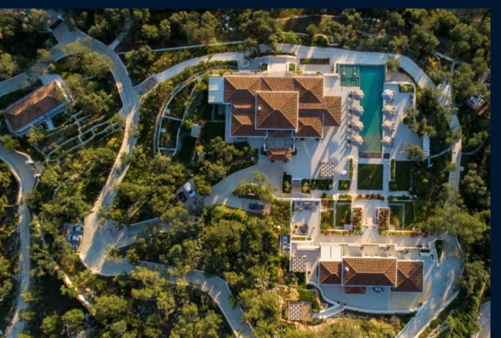 The estate from above in golden light, tiled roofs, pool and lawns, with white drives winding through the olive groves.